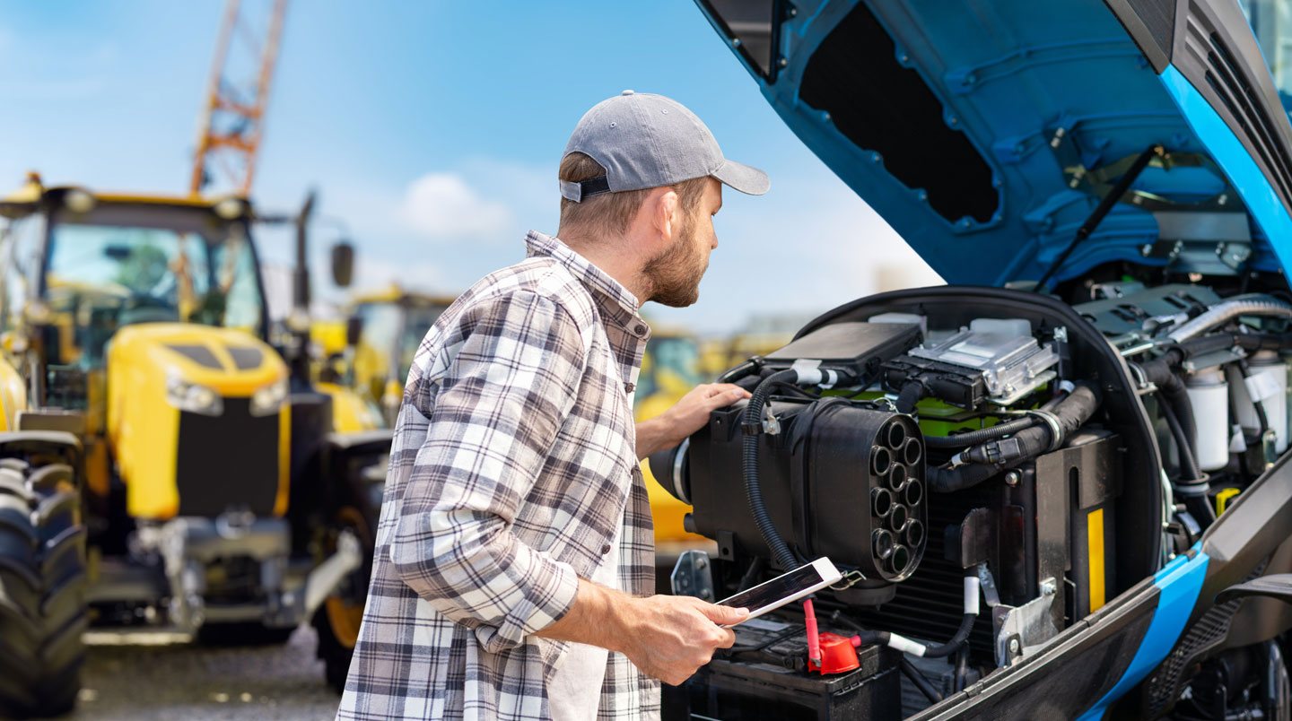 Technicien spécialisé inspectant un tracteur d'occasion avec son carnet d'entretien pour évaluer la fiabilité et la valeur de l'équipement